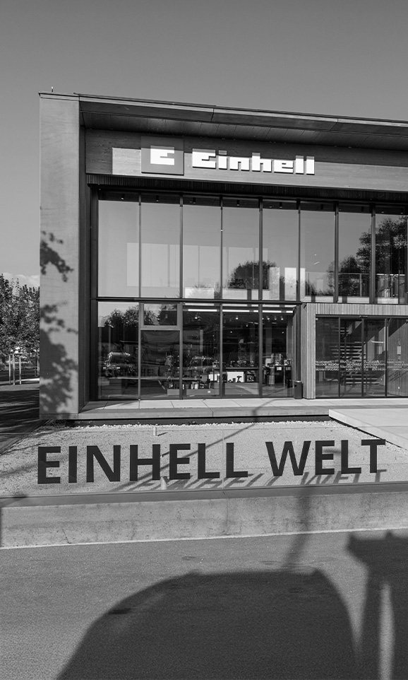 Svartvit bild på Einhell World: en modern företagsbyggnad med Einhell-logotypen och en stor grupp anställda.