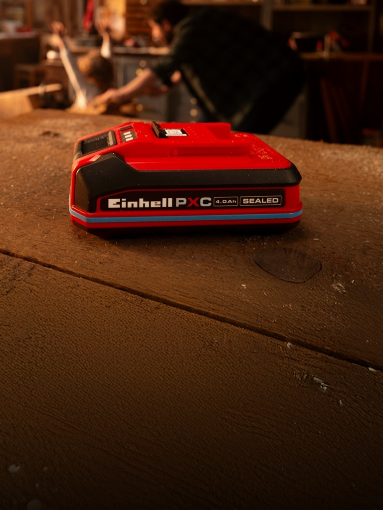 Einhell Power X-Change 4,0 Ah SEALEAD-batteri på en arbetsbänk i trä, med blå ring och etikett synlig.