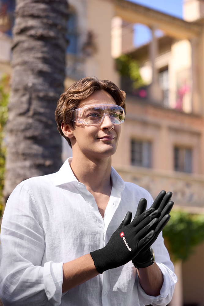 George Russell bär skyddsglasögon och Einhell-handskar medan han står i solen framför en villa.