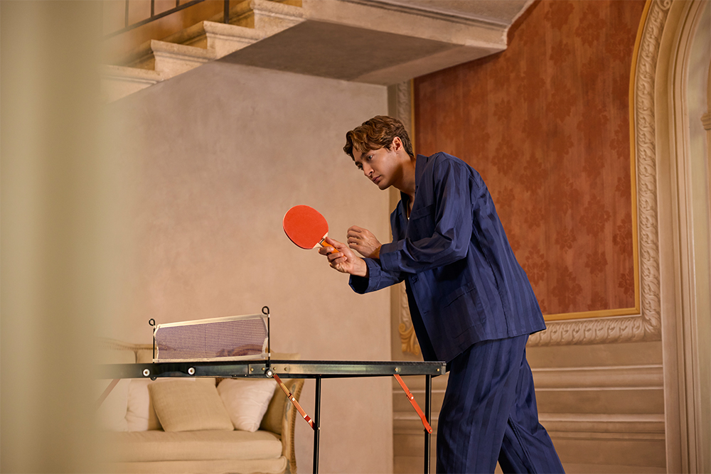 George Russell spelar bordtennis i ett rum med röd tapet och klassisk interiördesign.