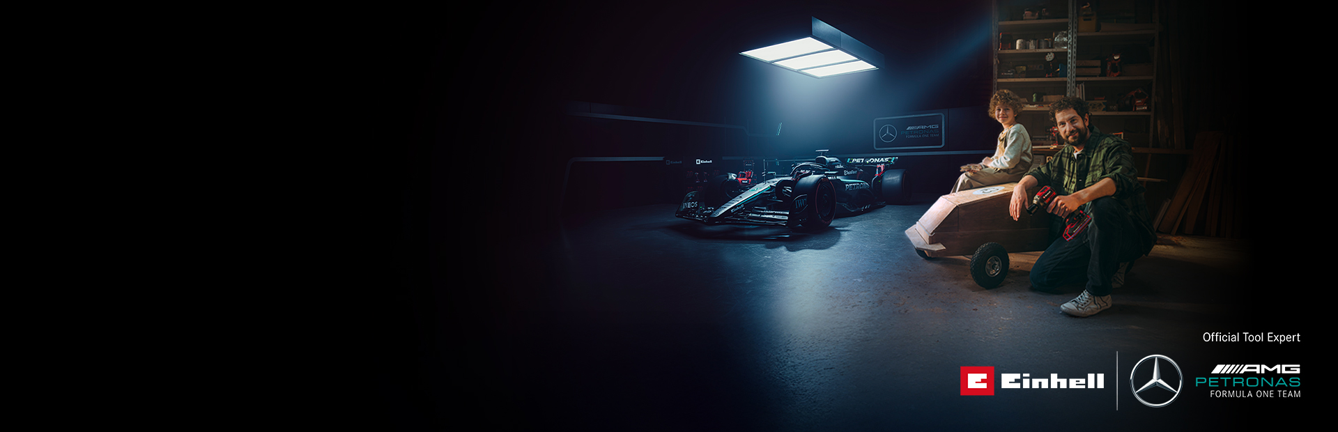 En pappa och ett barn i en verkstad med en hemmabyggd lådbil. I bakgrunden syns en Mercedes-AMG PETRONAS Formel 1-bil och verktyg från Einhell.