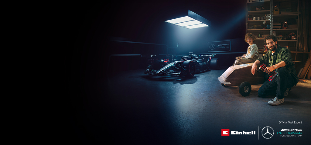 En pappa och ett barn i en verkstad med en hemmabyggd lådbil. I bakgrunden syns en Mercedes-AMG PETRONAS Formel 1-bil och verktyg från Einhell.