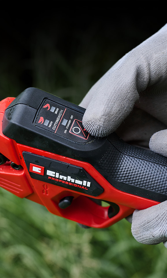 Närbild på en röd Einhell sladdlös produkt med en handskbeklädd hand som justerar dess läge.