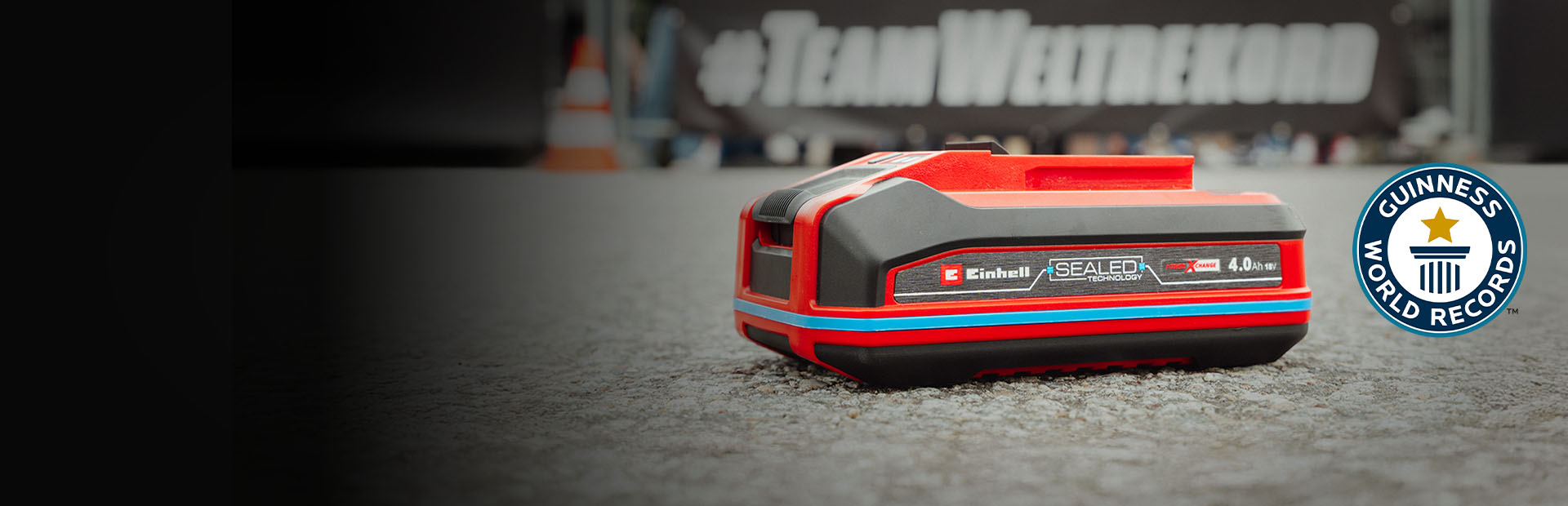 Einhell SEALED-batteri Power X-Change 4,0 Ah ligger på asfalt, med Guinness World Records logotyp ”Record Holder” till höger.