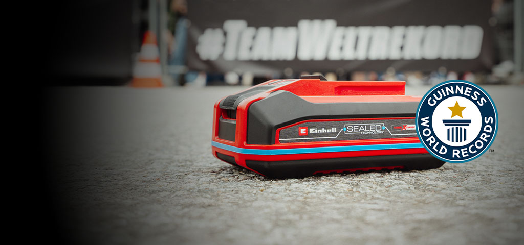Einhell SEALED-batteri Power X-Change 4,0 Ah ligger på asfalt, med Guinness World Records logotyp ”Record Holder” till höger.