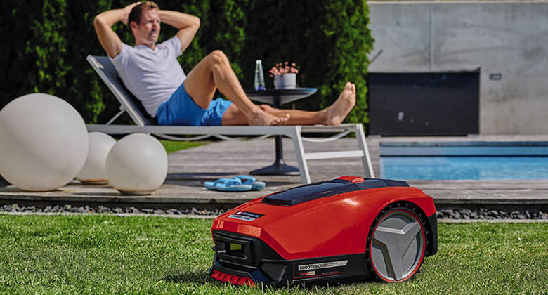 Robotic lawn mower in the garden, person relaxing in the background